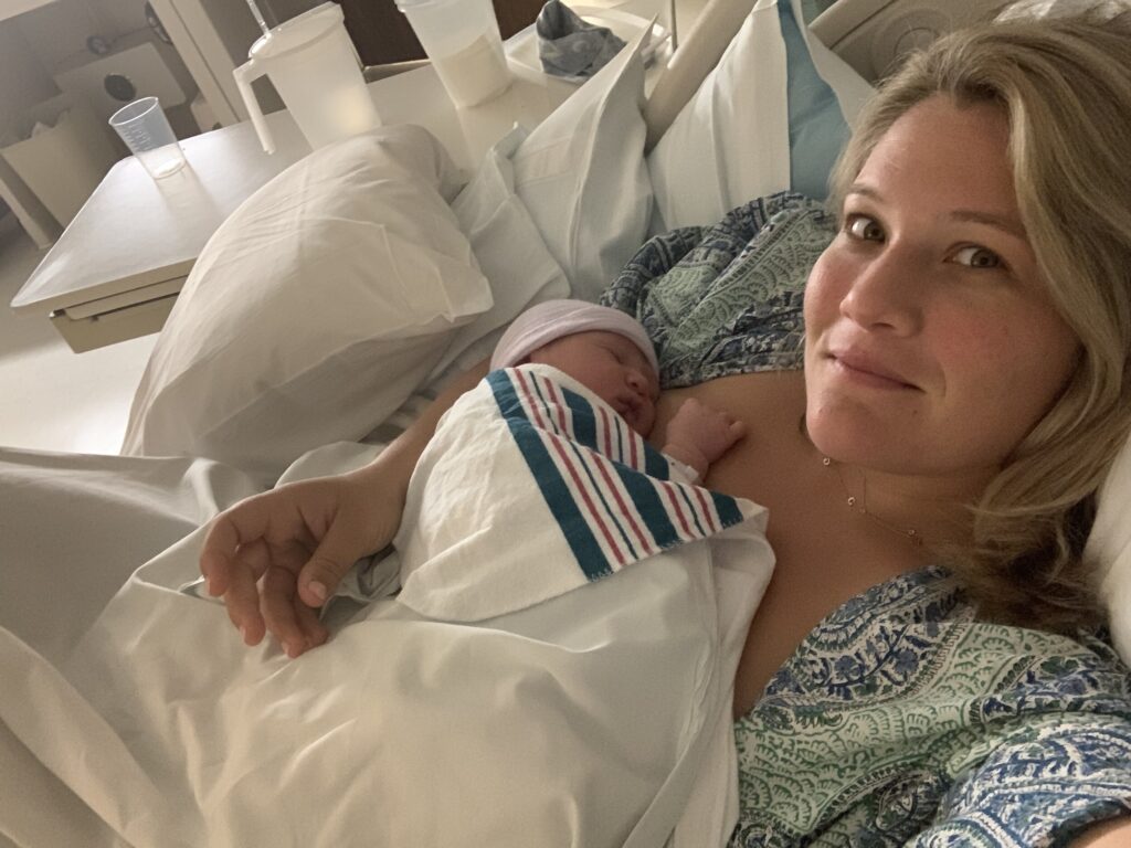 A woman lies in a hospital bed, holding a newborn baby wrapped in a blanket on her chest.