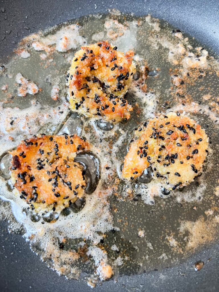 Three crispy sesame honey shrimp, breaded and fried with black sesame seeds, sizzle in a pan with oil and butter.