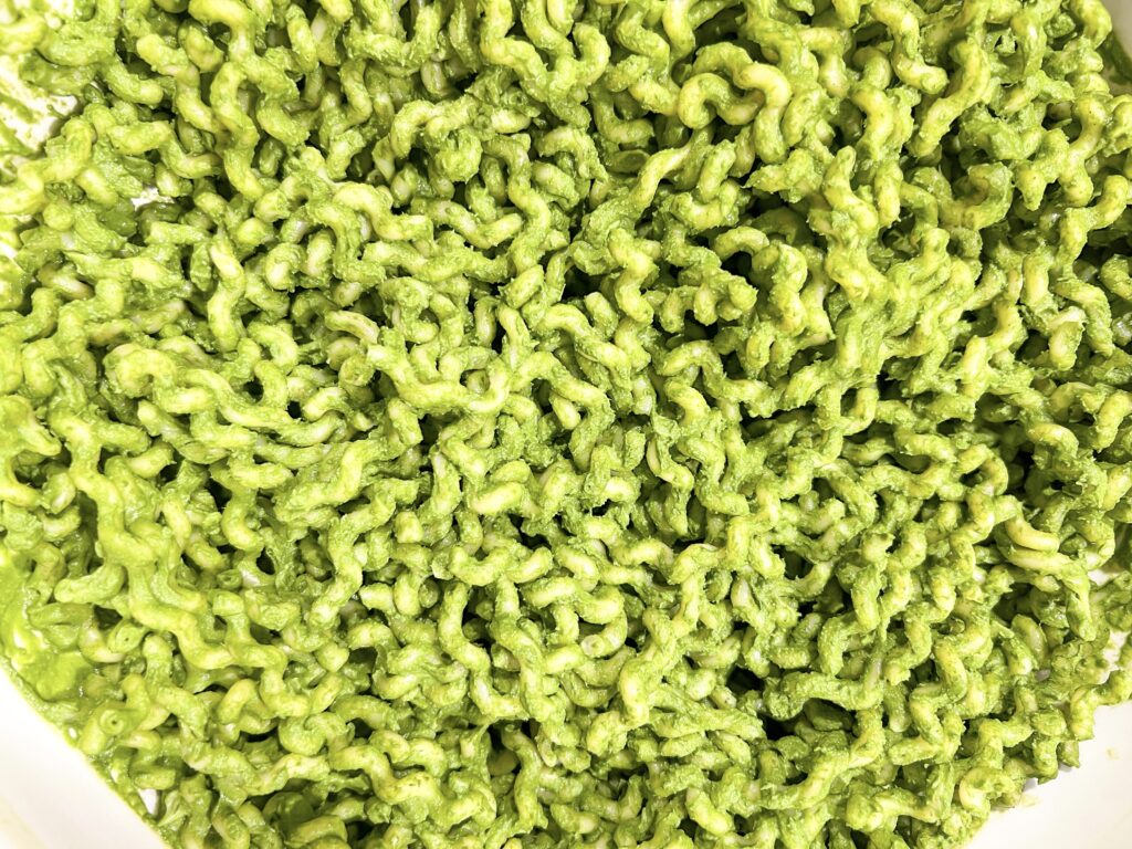 A close-up view of green, nutrient-dense pasta for the whole family, coated in vibrant pesto sauce.